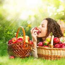Woman eating an apple on the grass with two apple baskets