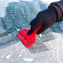 Hand in a glove scratching the frozen window with a red scraper