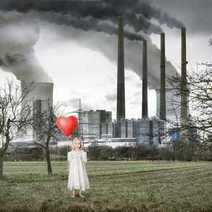 A little kid with a heart-shaped balloon with a big factory behind her