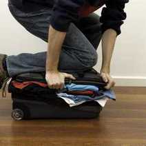 A guy trying to close his suitcase