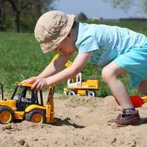 A boy pushing a tractor in a sandbox