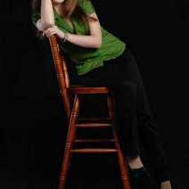 A girl in green shirt sitting on a bar chair and leaning on the rest