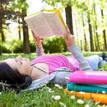 young woman laying on grass in the park and reading a book