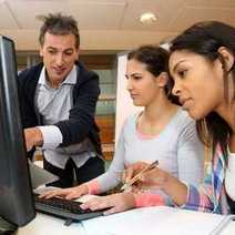 A boy giving instructions to two young ladies sitting on a computer